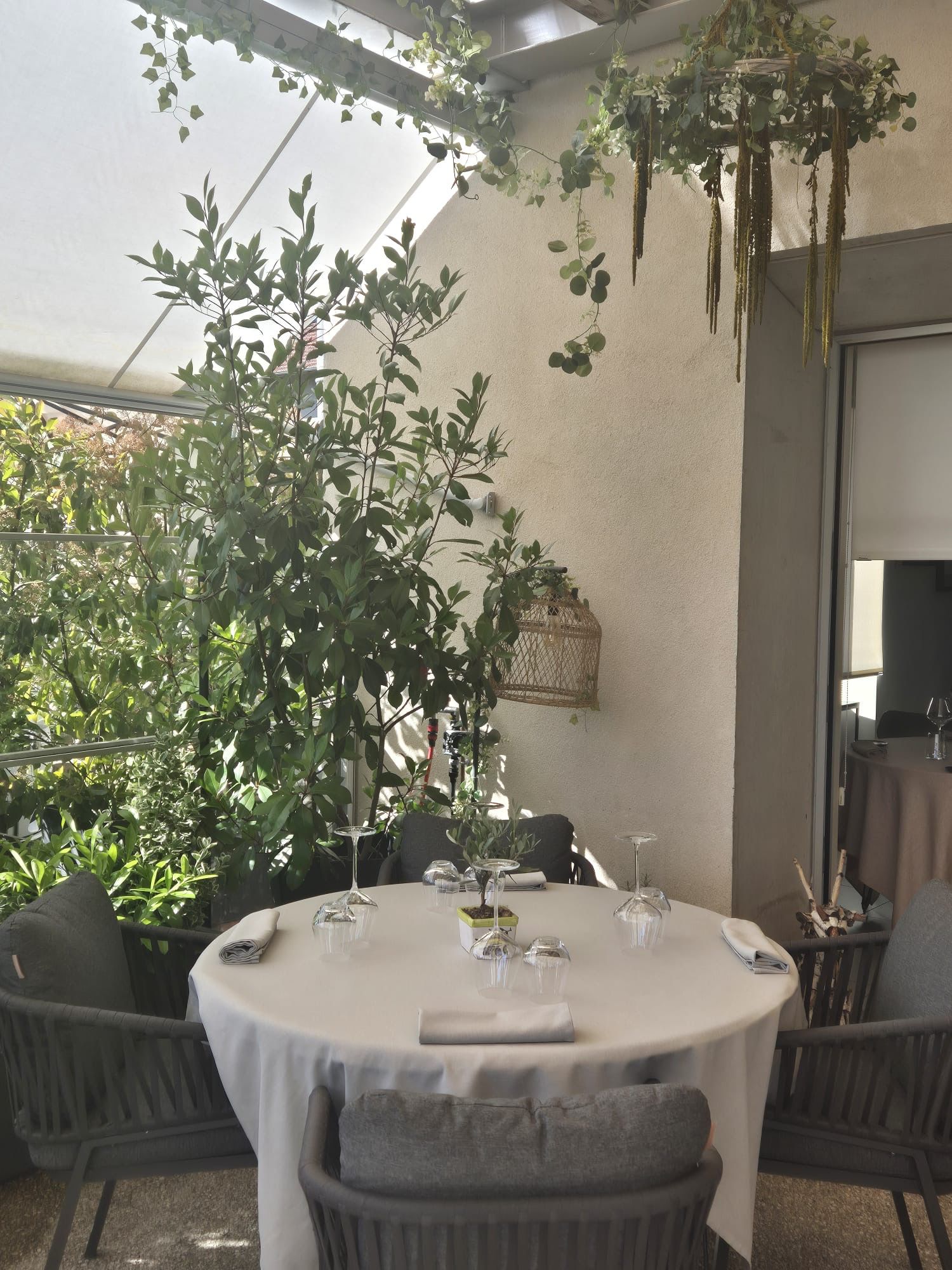 Table ronde dressée sur la terrasse de l'Auberge d'Arthaz, entourée d'oliviers et plantes suspendues