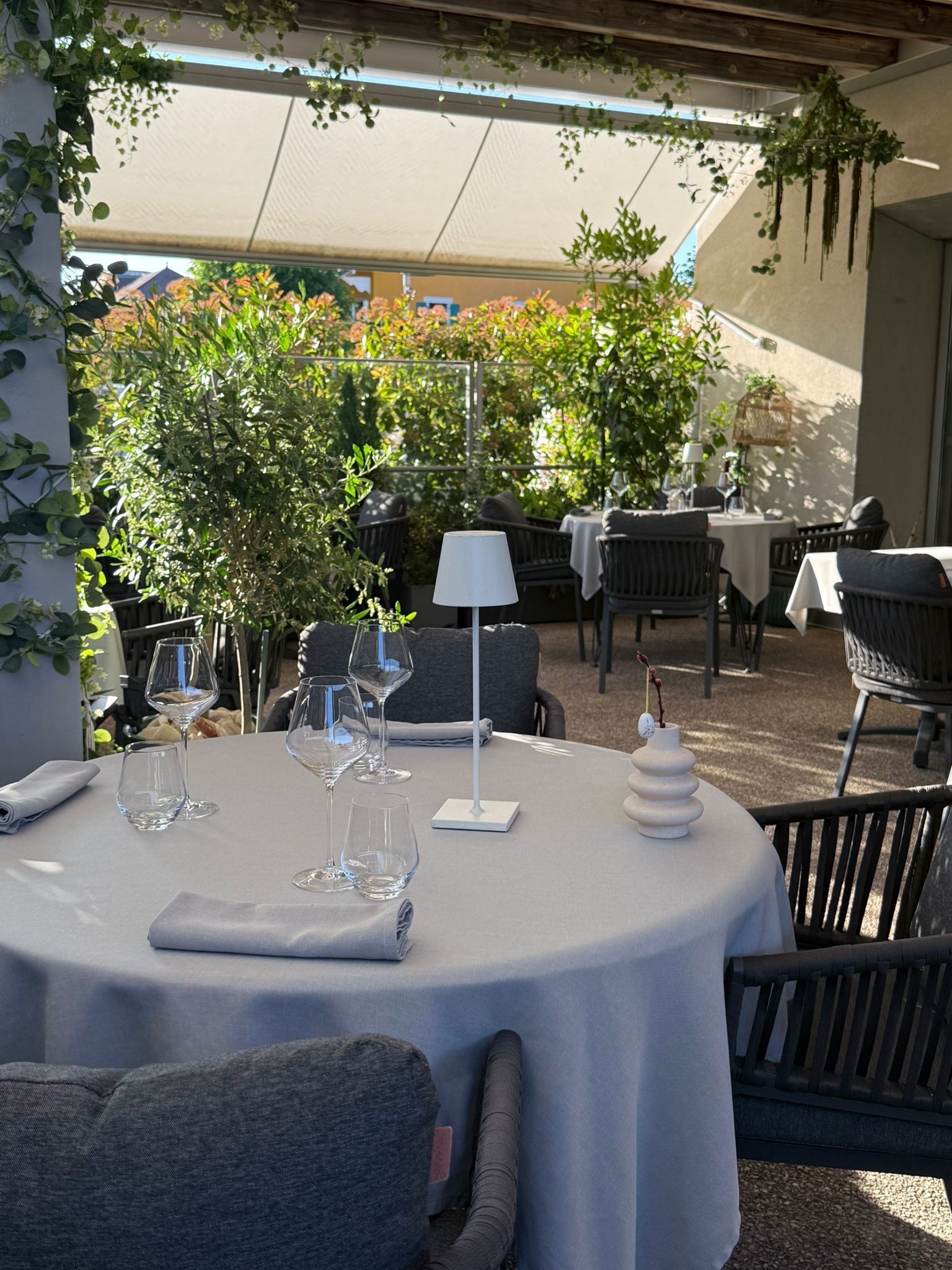 Vue d'ensemble de la terrasse couverte de l'Auberge d'Arthaz, plusieurs tables dressées sous auvent blanc en pleine lumière estivale