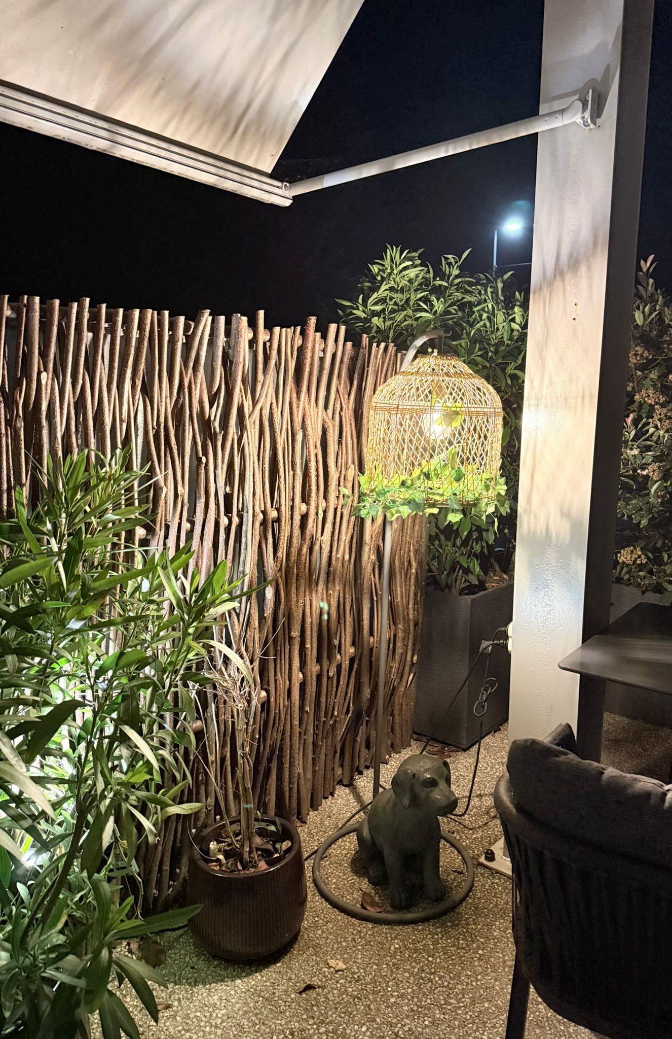 Coin terrasse de l'Auberge d'Arthaz la nuit, clôture en branches de noisetier, lampe en rotin allumée et figurine chien